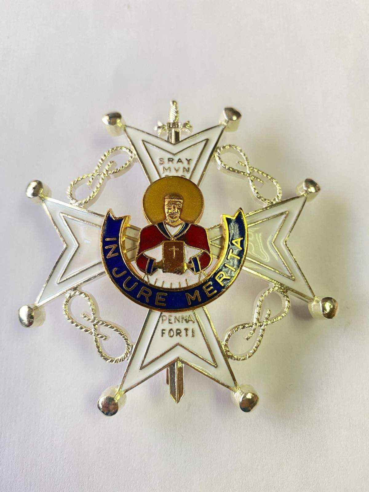 Medalla decorativa plateada en forma de estrella con emblema central y banderín azul sobre fondo blanco.