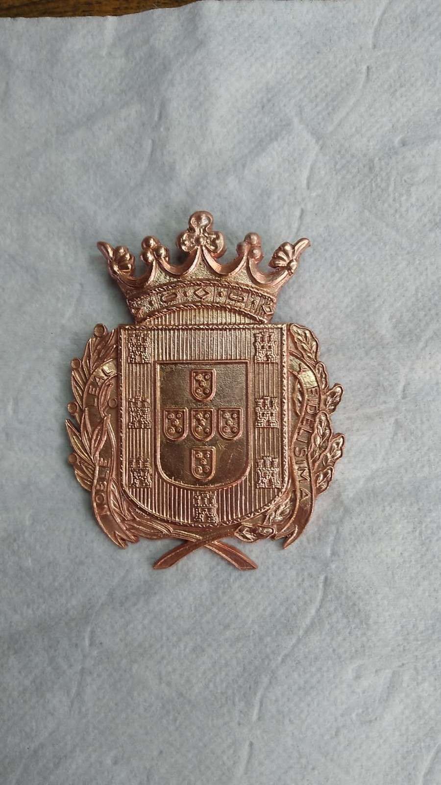 Escudo bordado de color cobre con una corona y un escudo sobre tela azul claro.