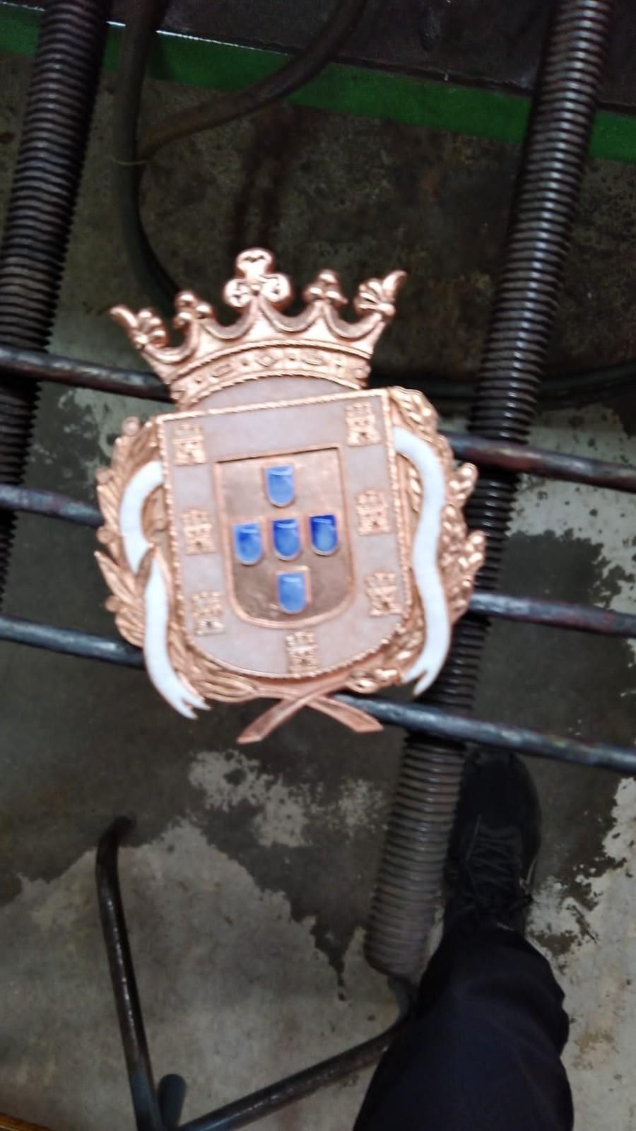 Un escudo coronado de color dorado y azul montado sobre una puerta o valla de metal.