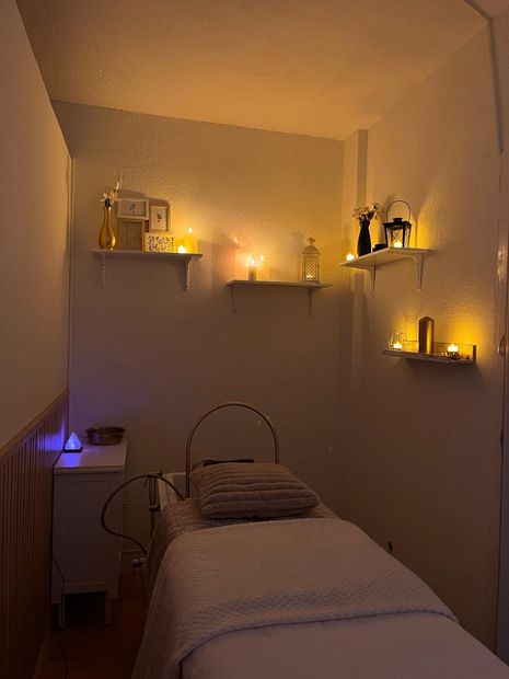 Acogedora habitación de spa con una cama estrecha, cálidas estanterías en la pared y velas brillantes en una suave luz ámbar.