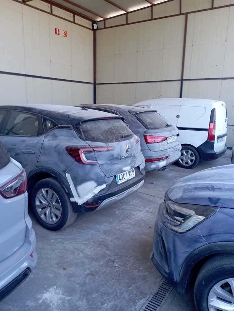 Dos caravanas blancas estacionadas en un lote de grava bajo un cielo azul con árboles.