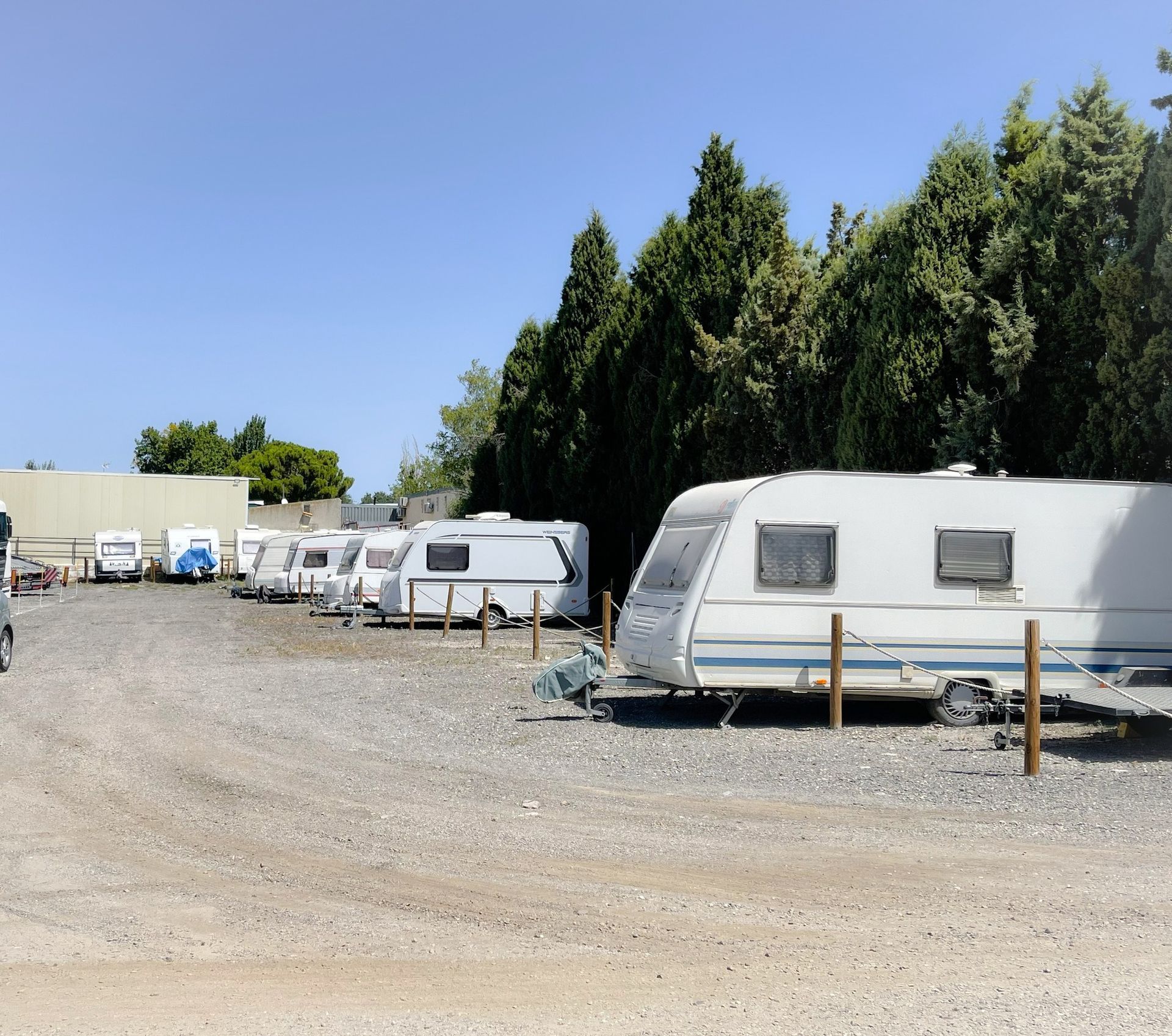 Caravanas estacionadas sobre grava en un terreno soleado, con árboles al fondo.