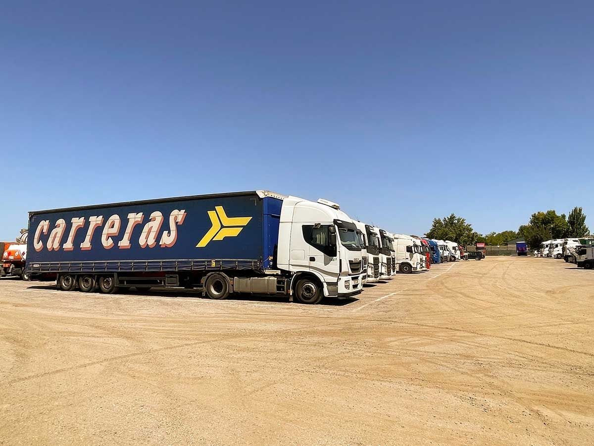 Camiones estacionados en un terreno de tierra bajo un cielo azul y despejado. El camión más grande lleva la inscripción