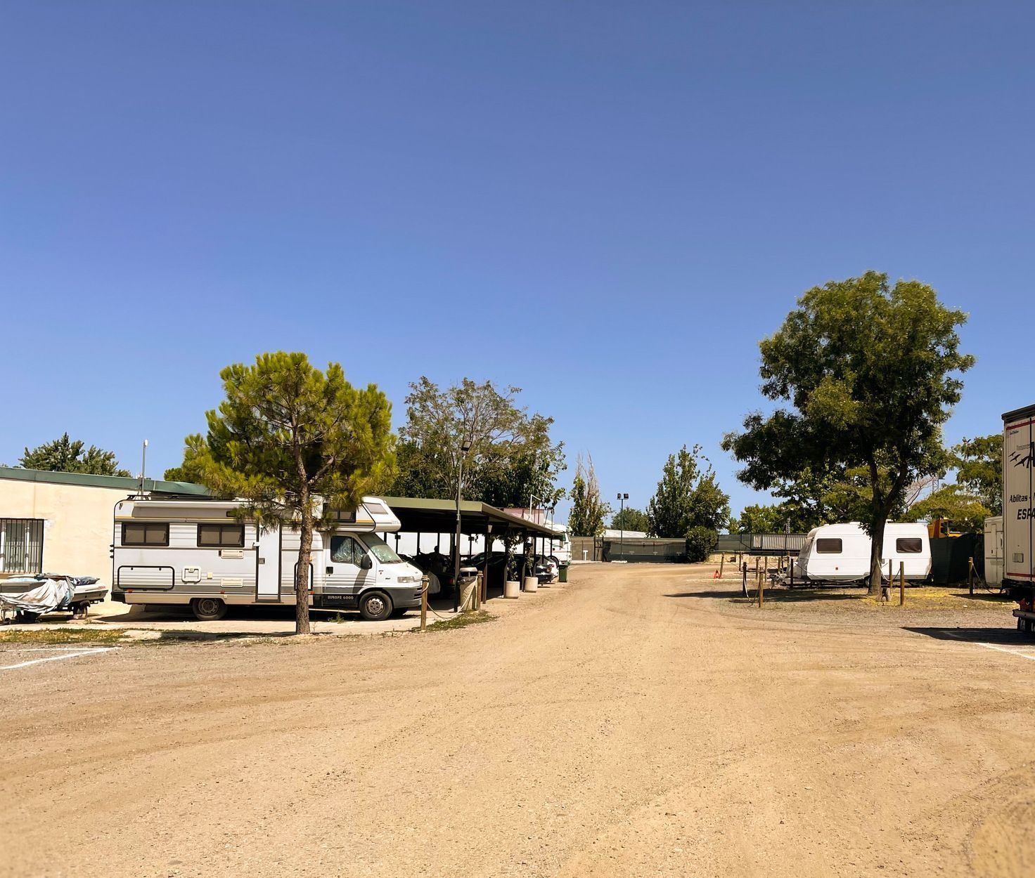Un parque de casas rodantes polvoriento con autocaravanas estacionadas bajo un cielo azul claro.