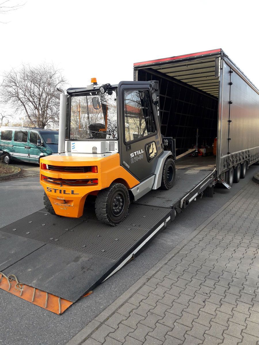 Ein orangefarbener und silberner Gabelstapler belädt auf einer Rampe einen Sattelauflieger.