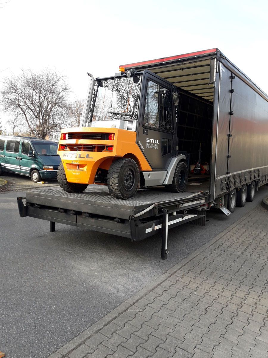 Ein orange-grauer Gabelstapler steht auf einer Laderampe und bereitet sich darauf vor, in einen Sattelauflieger einzufahren.