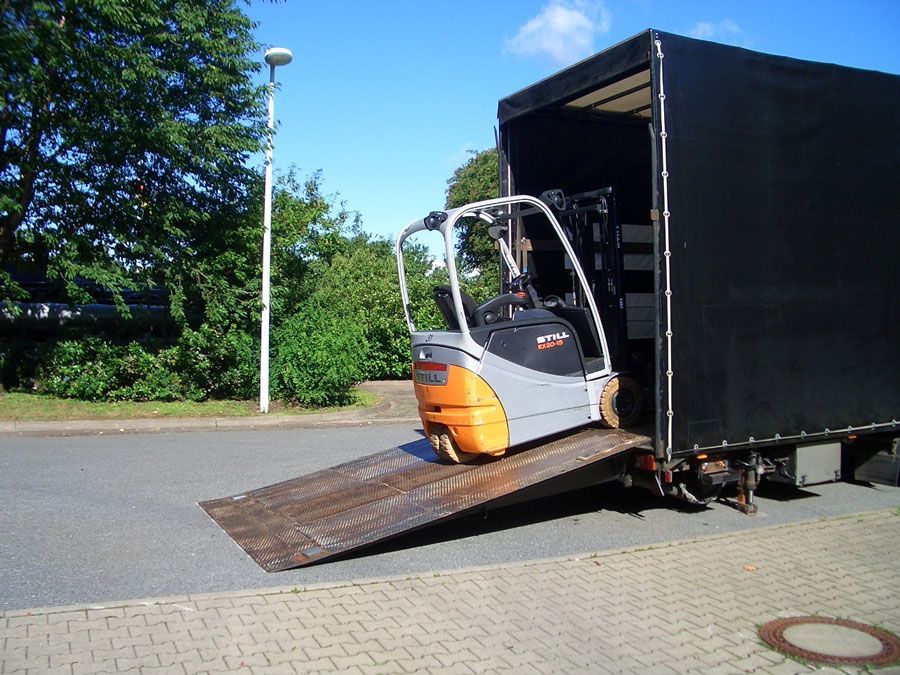 Gabelstapler auf der Rampe, Verladung in einen schwarzen Lastwagen, Außenaufnahme, sonniger Tag.