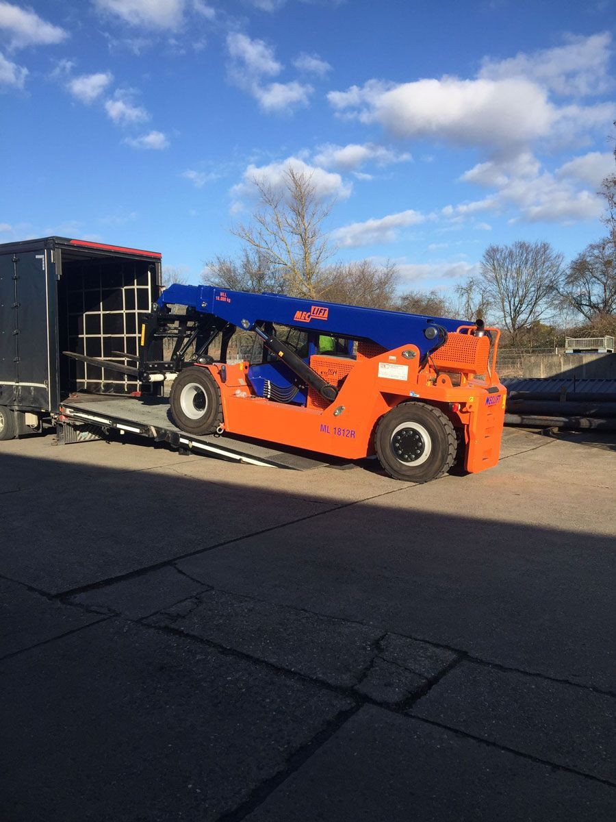 Ein orangefarbener und ein blauer Gabelstapler entladen an einem sonnigen Tag einen LKW.