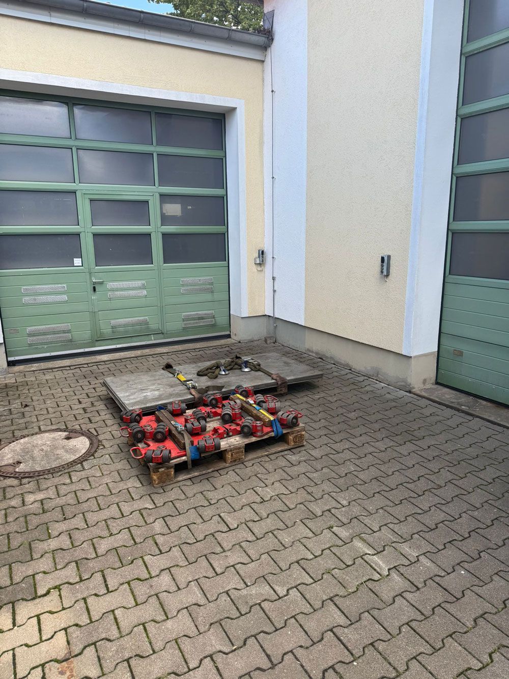 Grüne Garagentore, Betonpflastersteine, eine Palette roter Werkzeuge vor einem Gebäude.