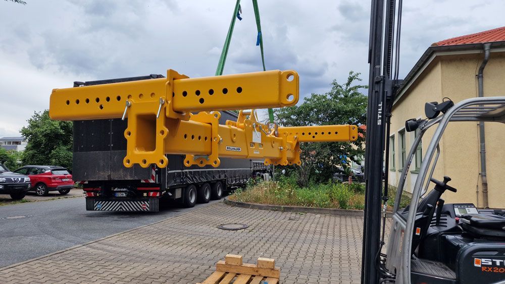 Ein gelbes Bauteil einer schweren Maschine wird mit einem Kran auf einen LKW gehoben.