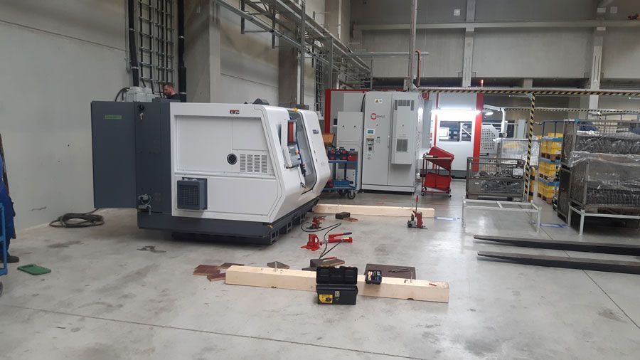 In einer Fabrik wird eine große Industriemaschine aufgebaut. Holzklötze und Werkzeuge liegen auf dem Boden.