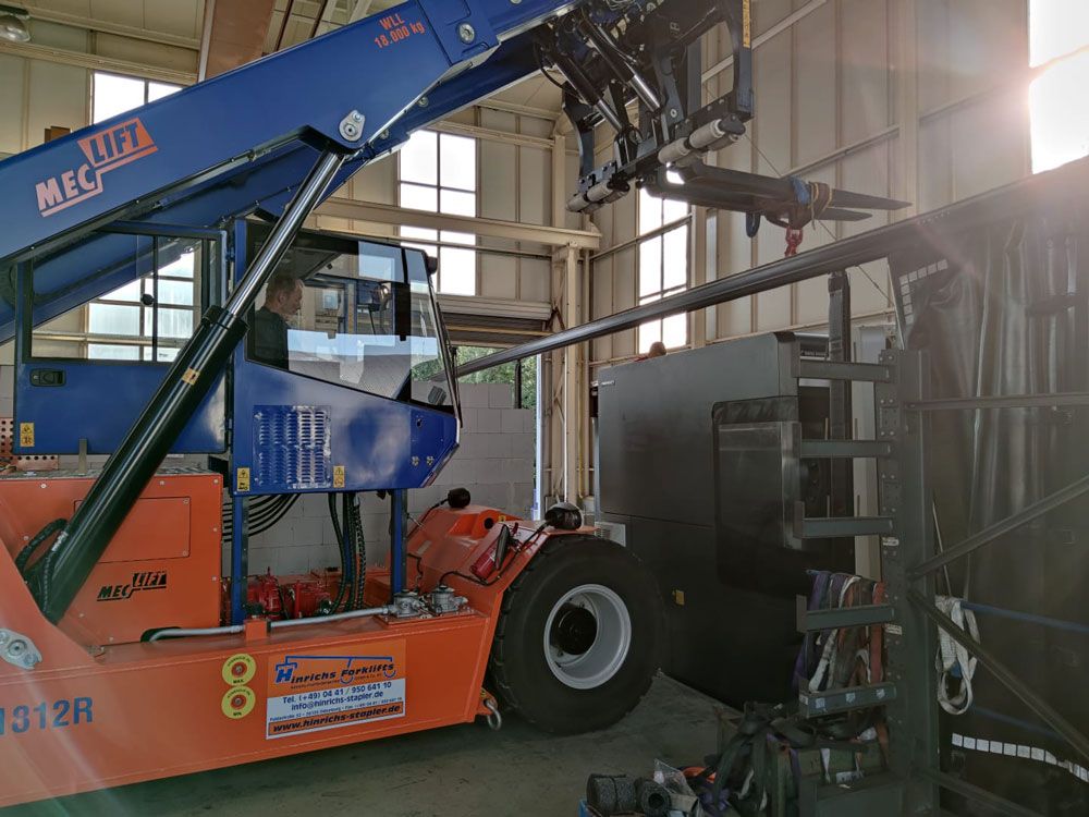 Ein orangefarbener und blauer Gabelstapler hebt eine Metallstange in einem Lagerhaus an.