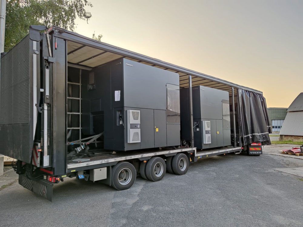 Zwei große schwarze Maschinen, verladen auf einen Sattelauflieger, der im Freien parkt.