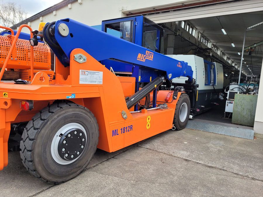 Ein orange-blaues Industriefahrzeug mit großen Rädern parkt unter dem Eingang eines Gebäudes.