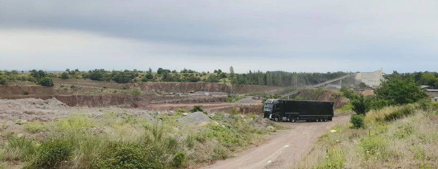 Ein dunkler Lastwagen auf einem Feldweg in einem Steinbruch, unter bedecktem Himmel.