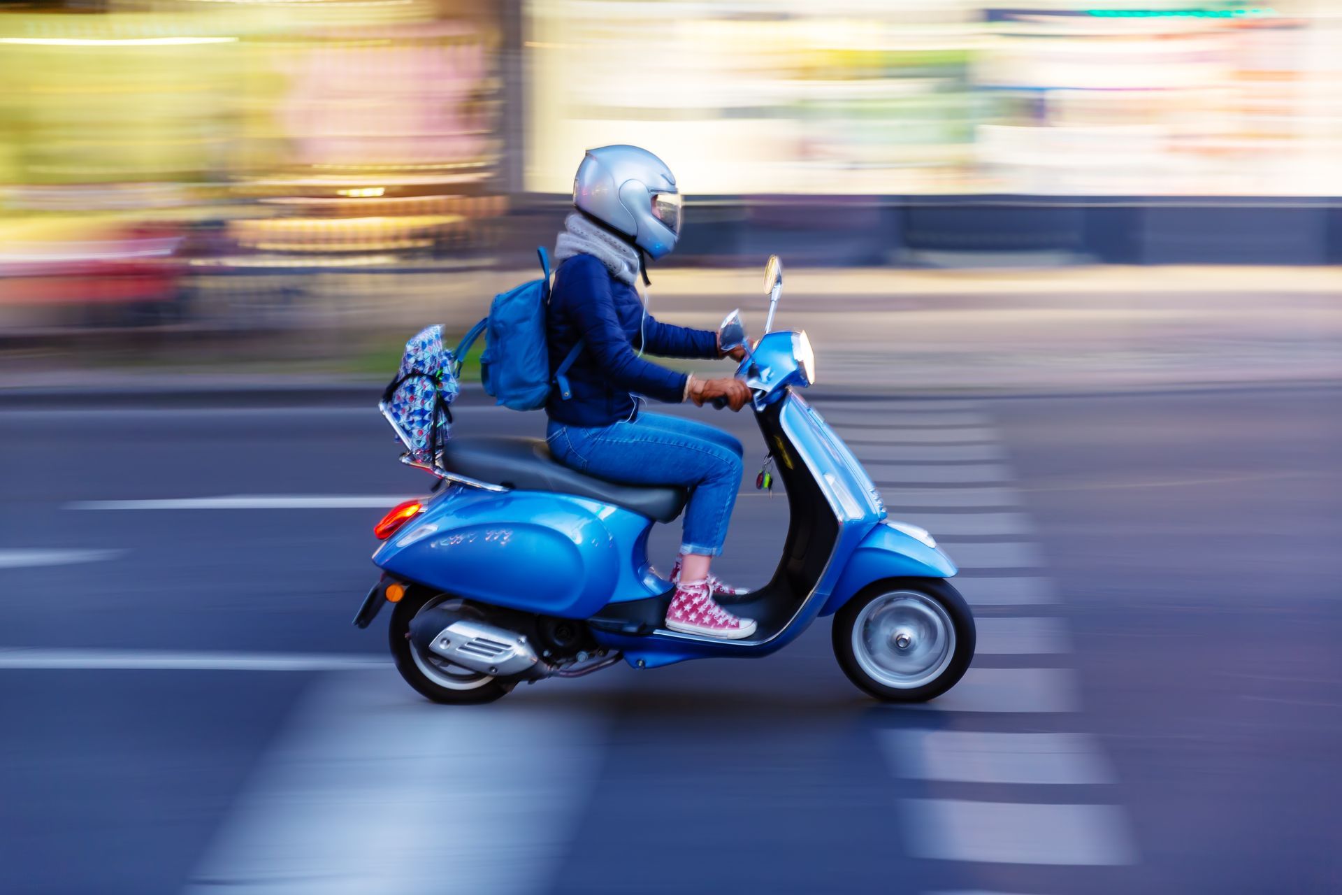 Personne sur un scooter bleu, portant un casque, circulant dans une rue de la ville.