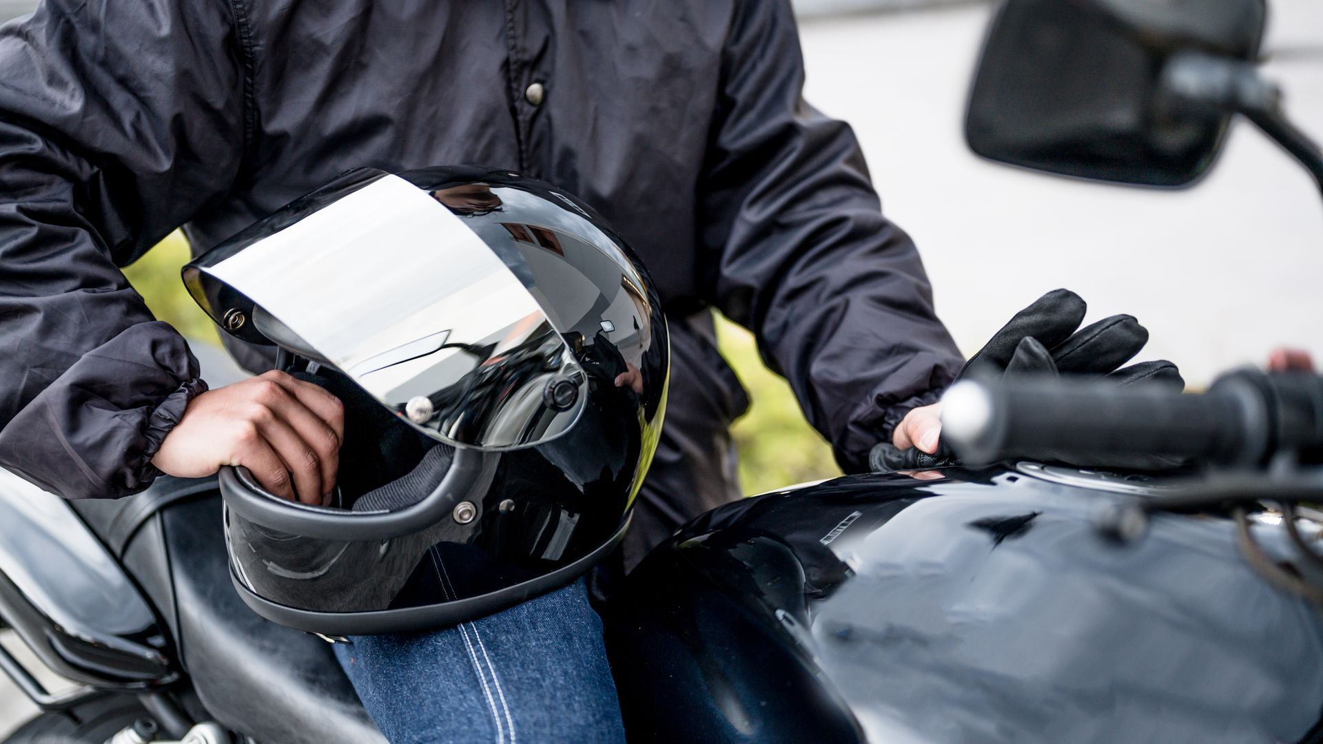 Personne tenant un casque de moto noir, assise sur une moto.