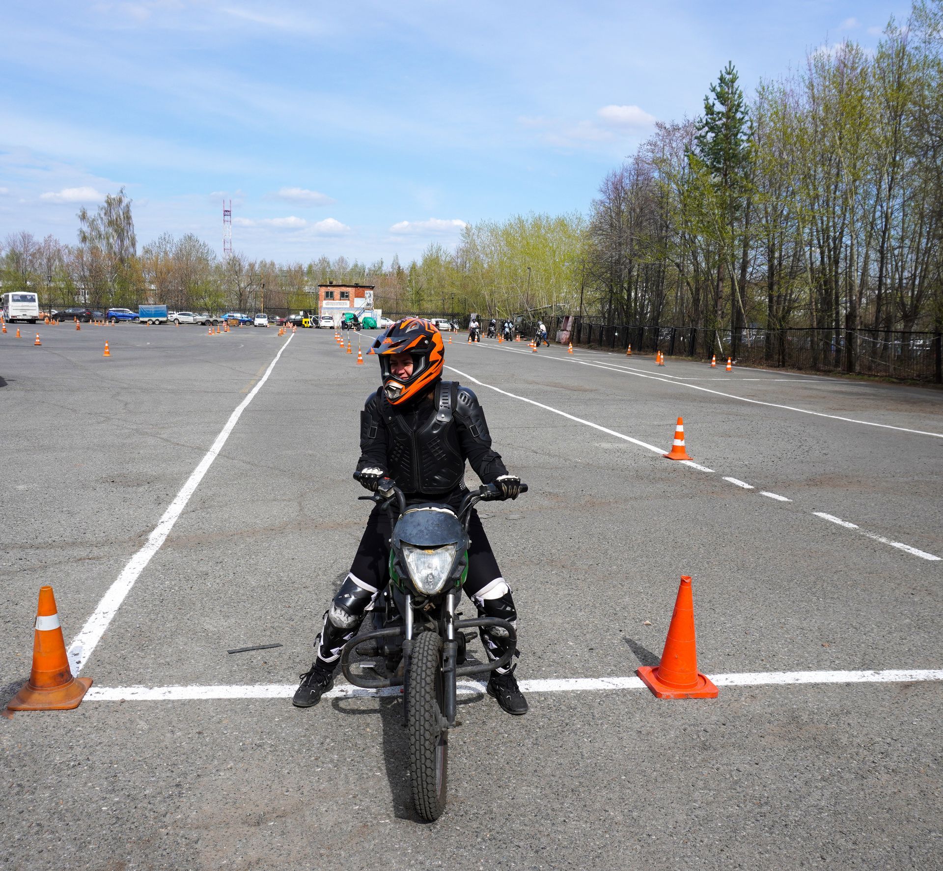 Motocycliste en équipement de sécurité sur une moto sur un circuit de conduite, entouré de cônes, sous un ciel bleu.
