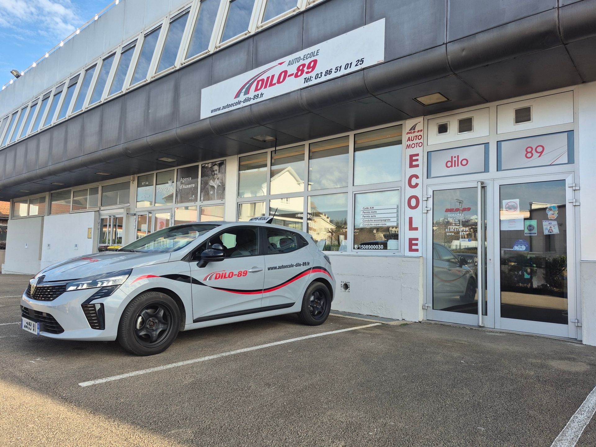 Voiture garée devant une boutique aux portes vitrées et une enseigne rouge et blanche au-dessus de l'entrée.