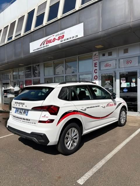 Un SUV blanc est stationné devant un bâtiment de service Ecolo 89 avec une signalétique rouge et noire.