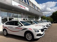 Voitures blanches garées devant une auto-école sous un ciel nuageux.