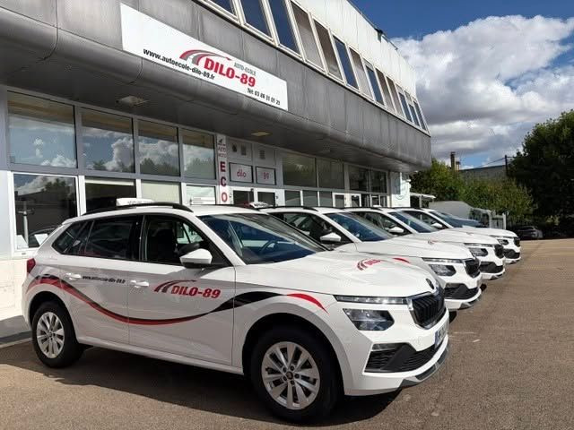Voitures de société blanches garées devant une auto-école sous un ciel nuageux.