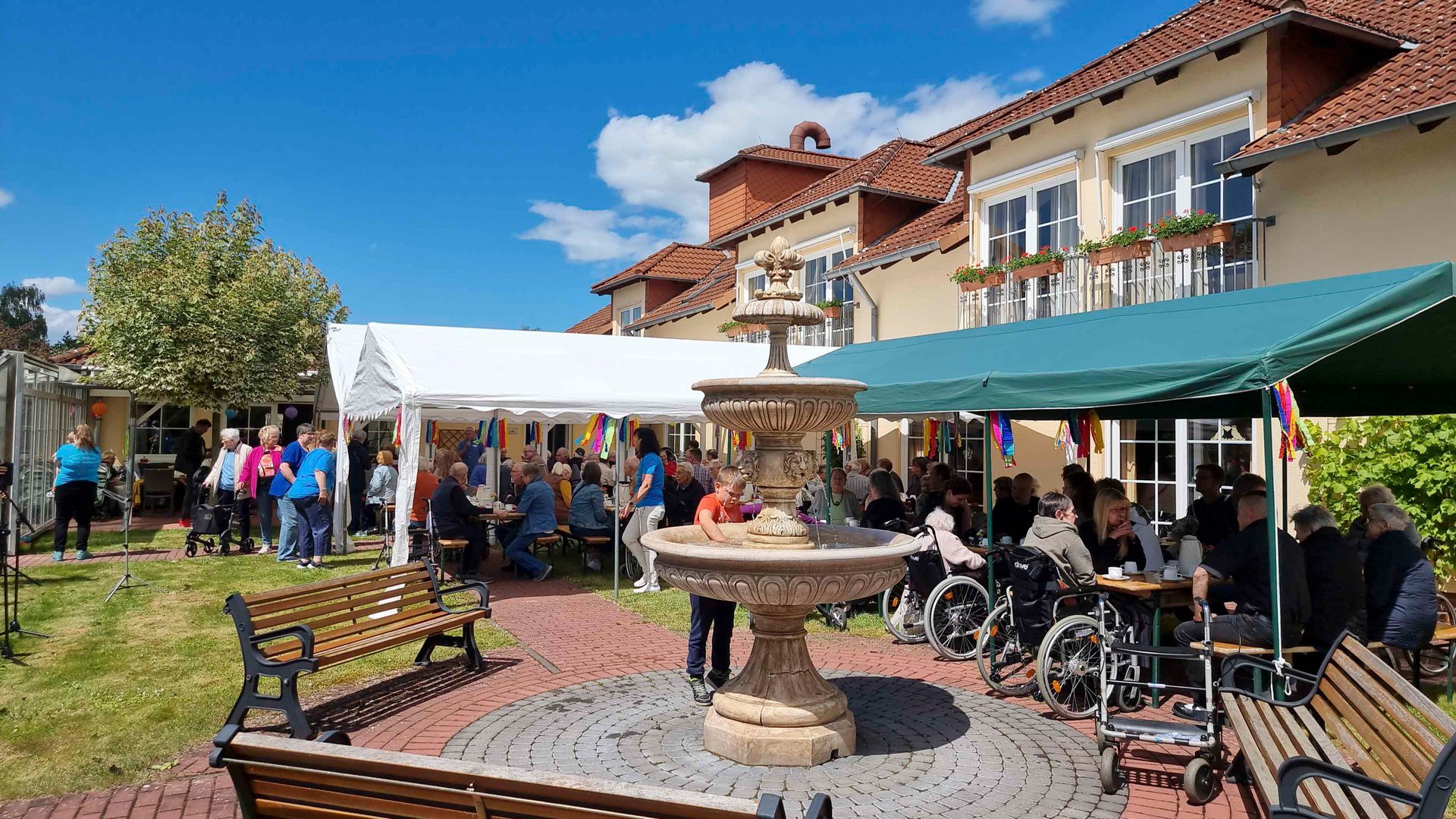 Eine Gruppe von Menschen sitzt um einen Brunnen vor einem Gebäude.