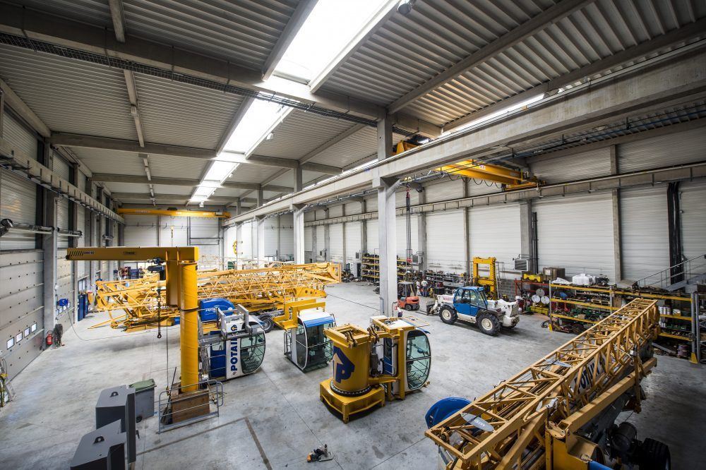 Grand atelier avec des engins de chantier jaunes, des ponts roulants et un petit véhicule bleu.
