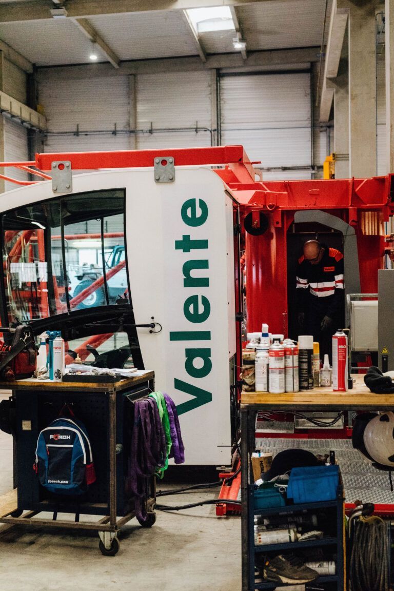 Une personne en uniforme rouge se tient à l'intérieur de la cabine rouge et blanche d'une machine Valente, dans un atelier.