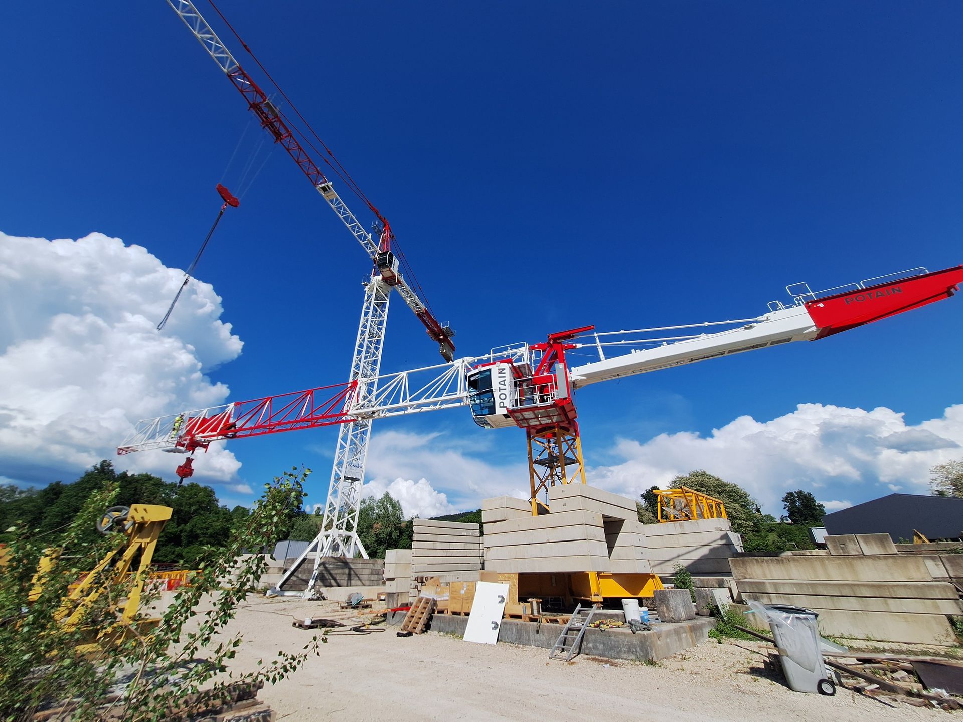 Deux grues de chantier rouges et blanches se détachant sur un ciel bleu, sur un chantier de construction.