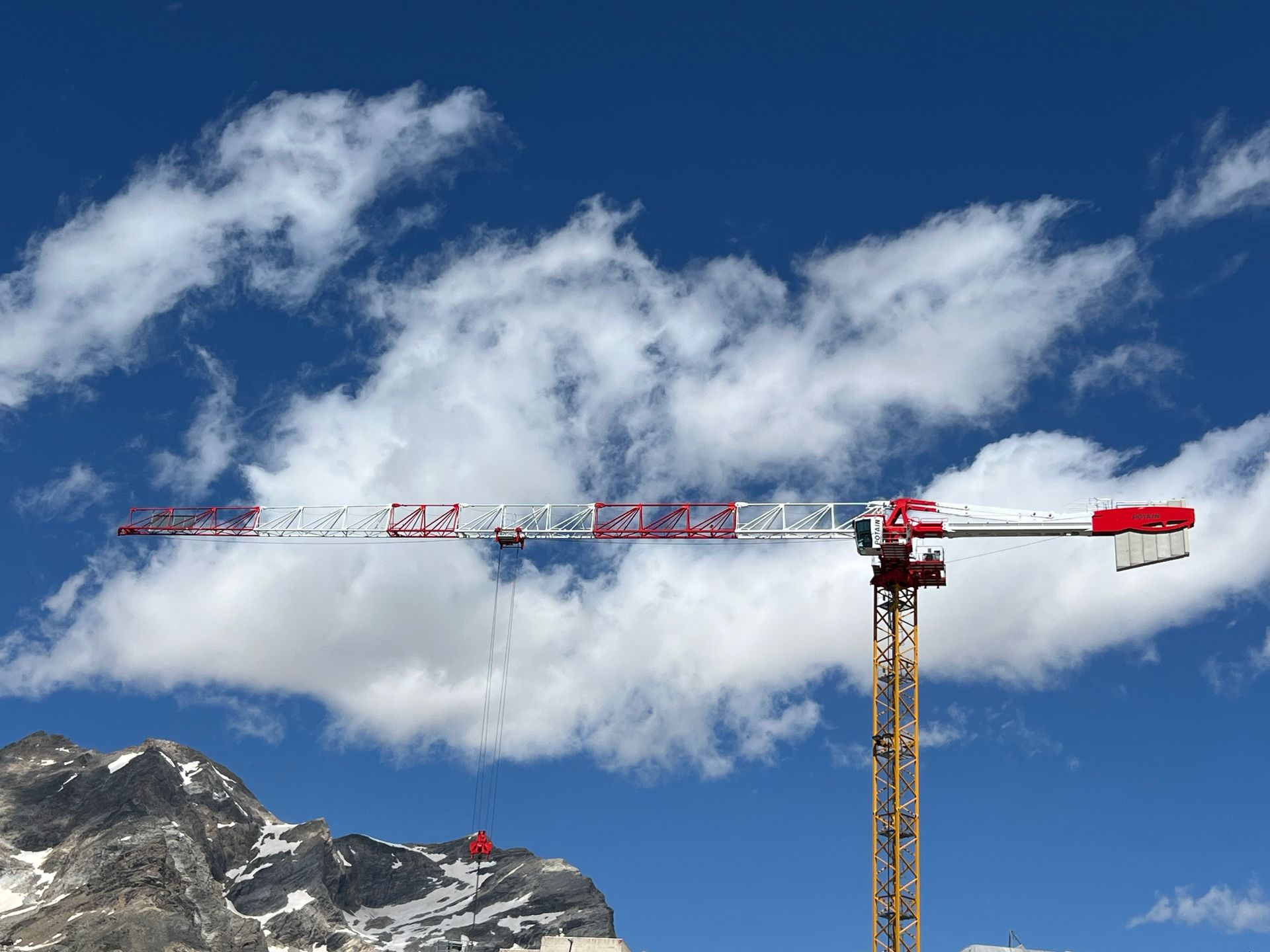 Grue de chantier se détachant sur un ciel bleu nuageux et une montagne enneigée.