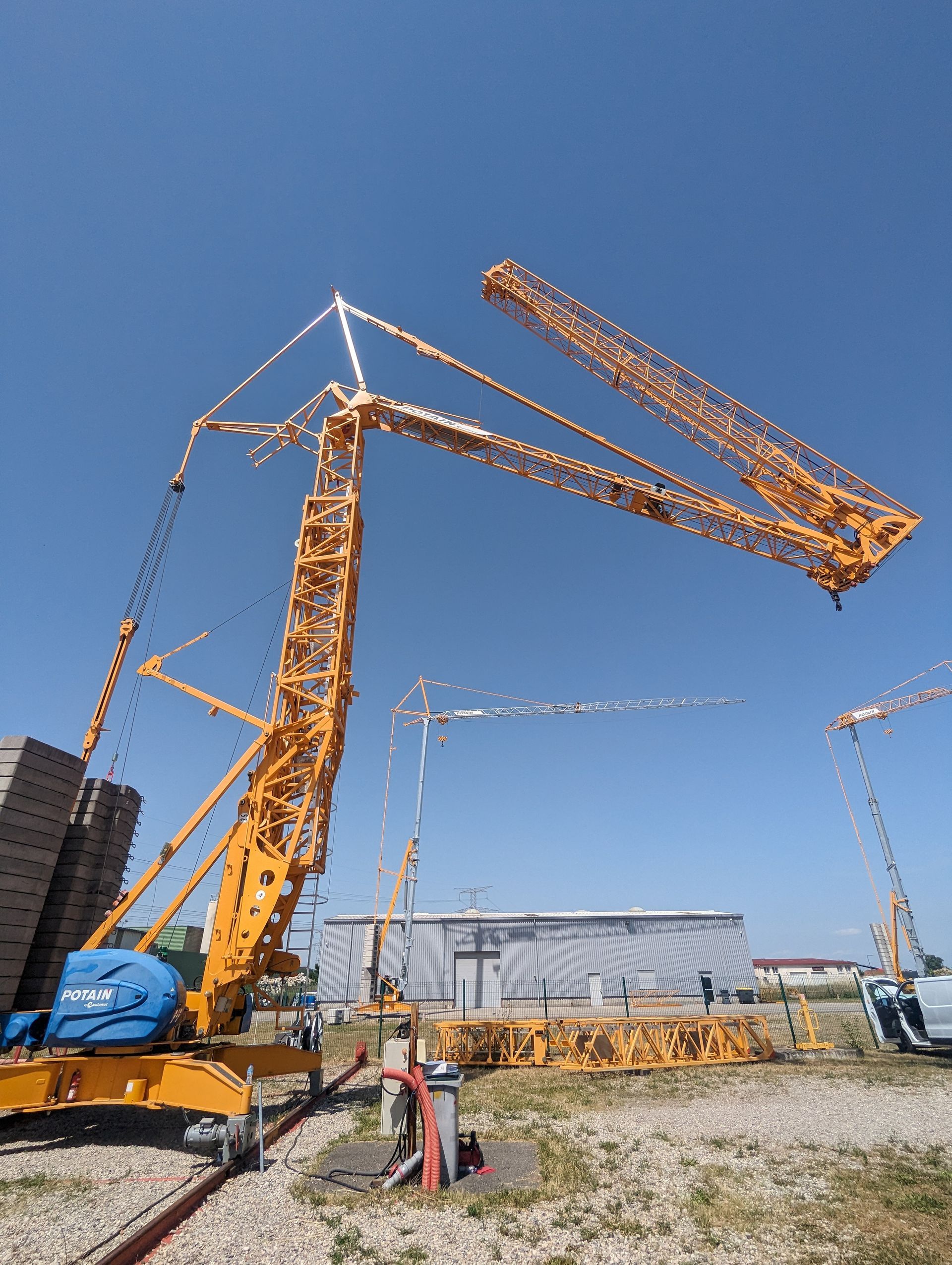 Grues de chantier jaunes se détachant sur un ciel bleu clair, au milieu d'un champ.