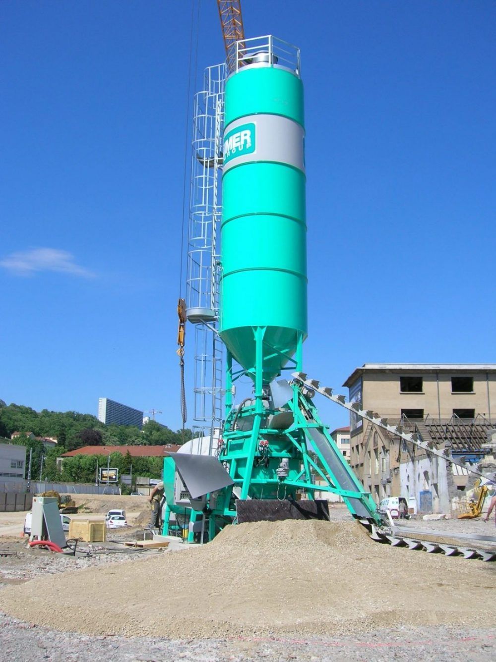 Centrale à béton verte sur un chantier de construction sous un ciel bleu.