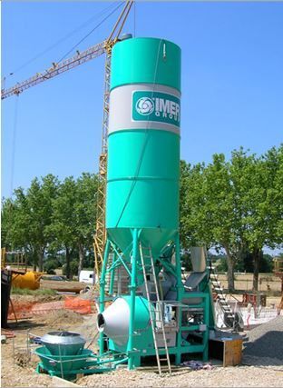 Centrale à béton vert et gris sur un chantier de construction, avec une grue en arrière-plan.