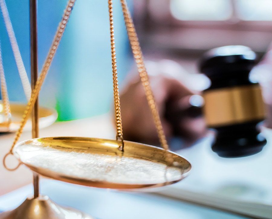 Balanza de la justicia enfocada con un mazo al fondo. Colores dorado y negro.