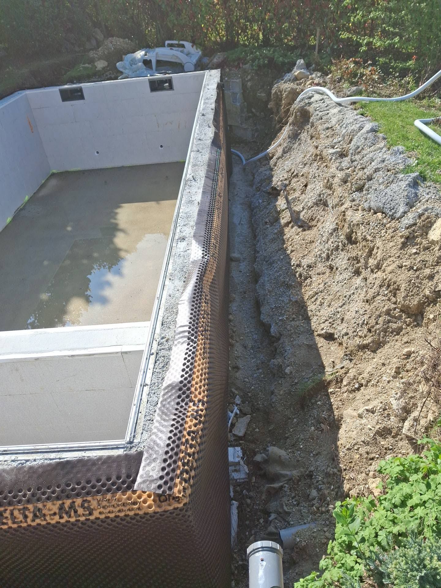 Piscine en béton partiellement construite à côté d'un fossé en terre, avec excavation le long.