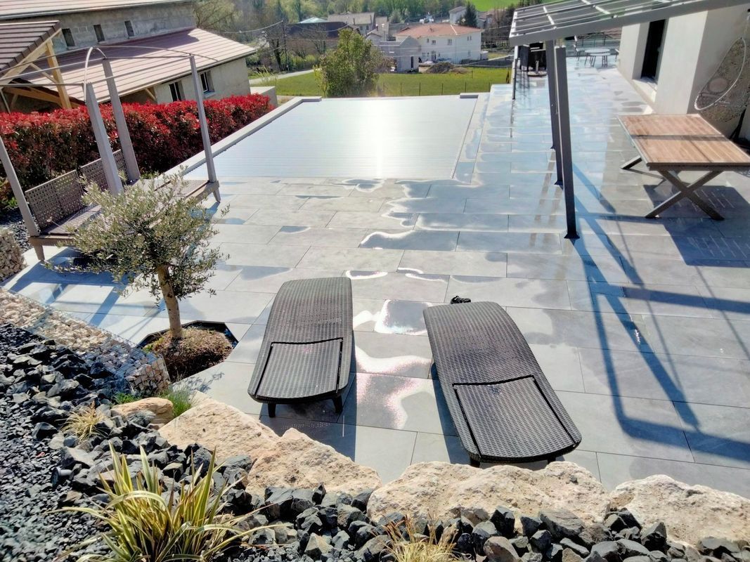 Terrasse avec piscine à débordement, deux chaises longues, aménagement paysager en pierre.