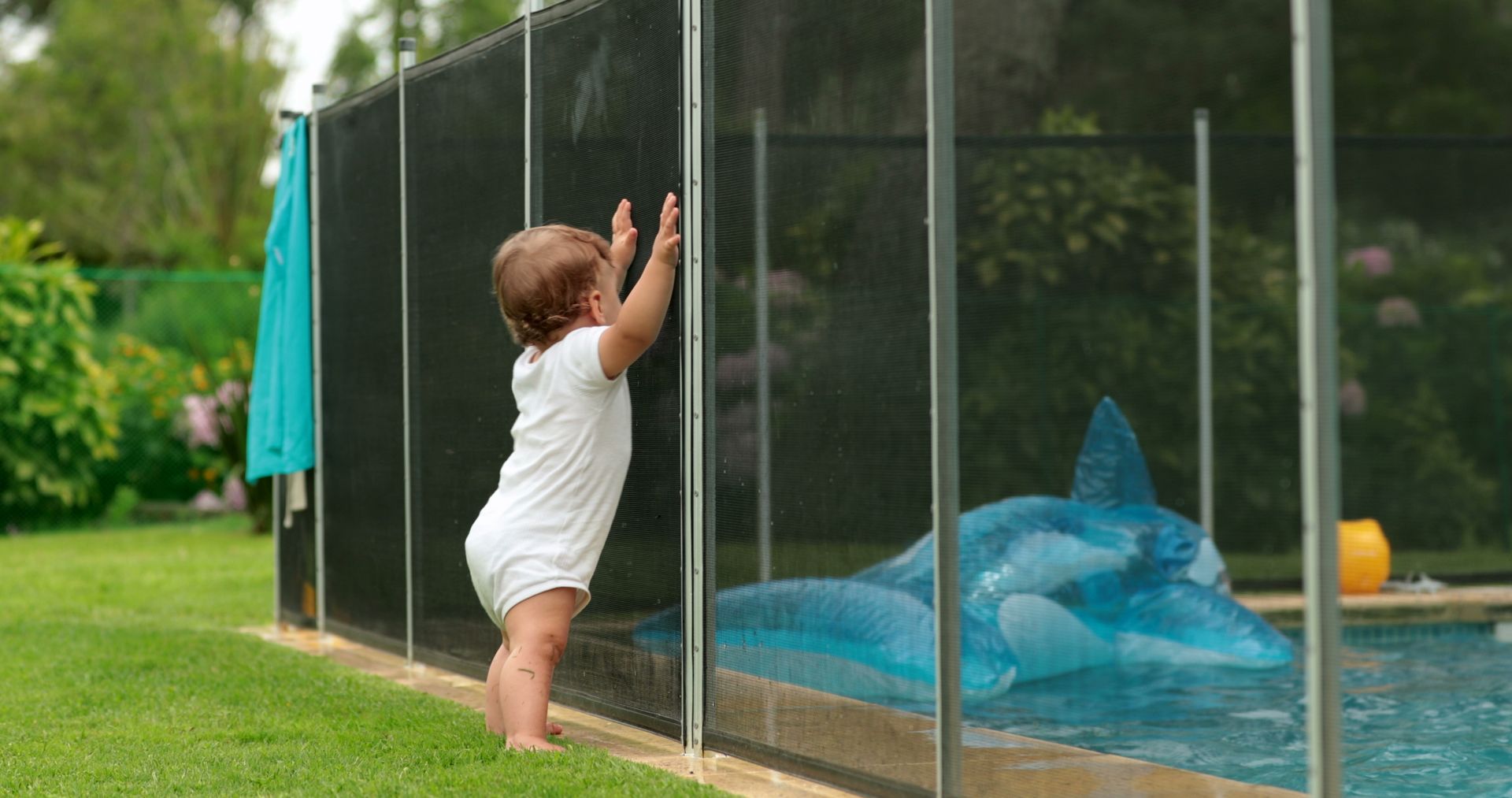 Un bébé se tient près de la clôture de la piscine.