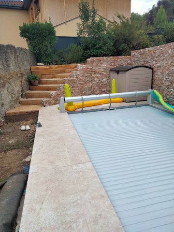 Espace piscine dans la cour arrière avec marches, mur en pierre et piscine hors sol couverte.