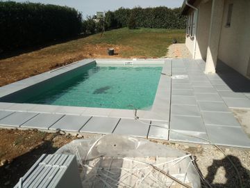 Cour arrière avec une petite piscine turquoise à côté d'une terrasse carrelée de gris.