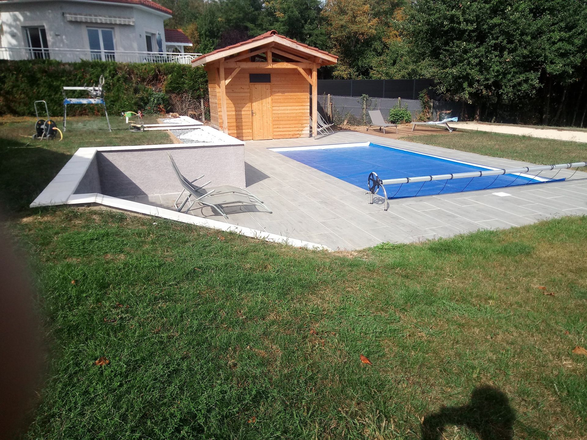 Piscine dans un jardin avec bâche bleue et abri de jardin en bois.
