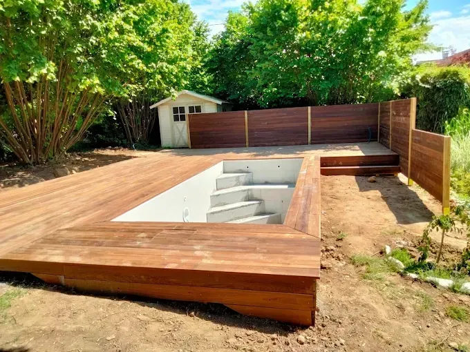 Terrasse en bois avec piscine creusée en construction dans une cour arrière.