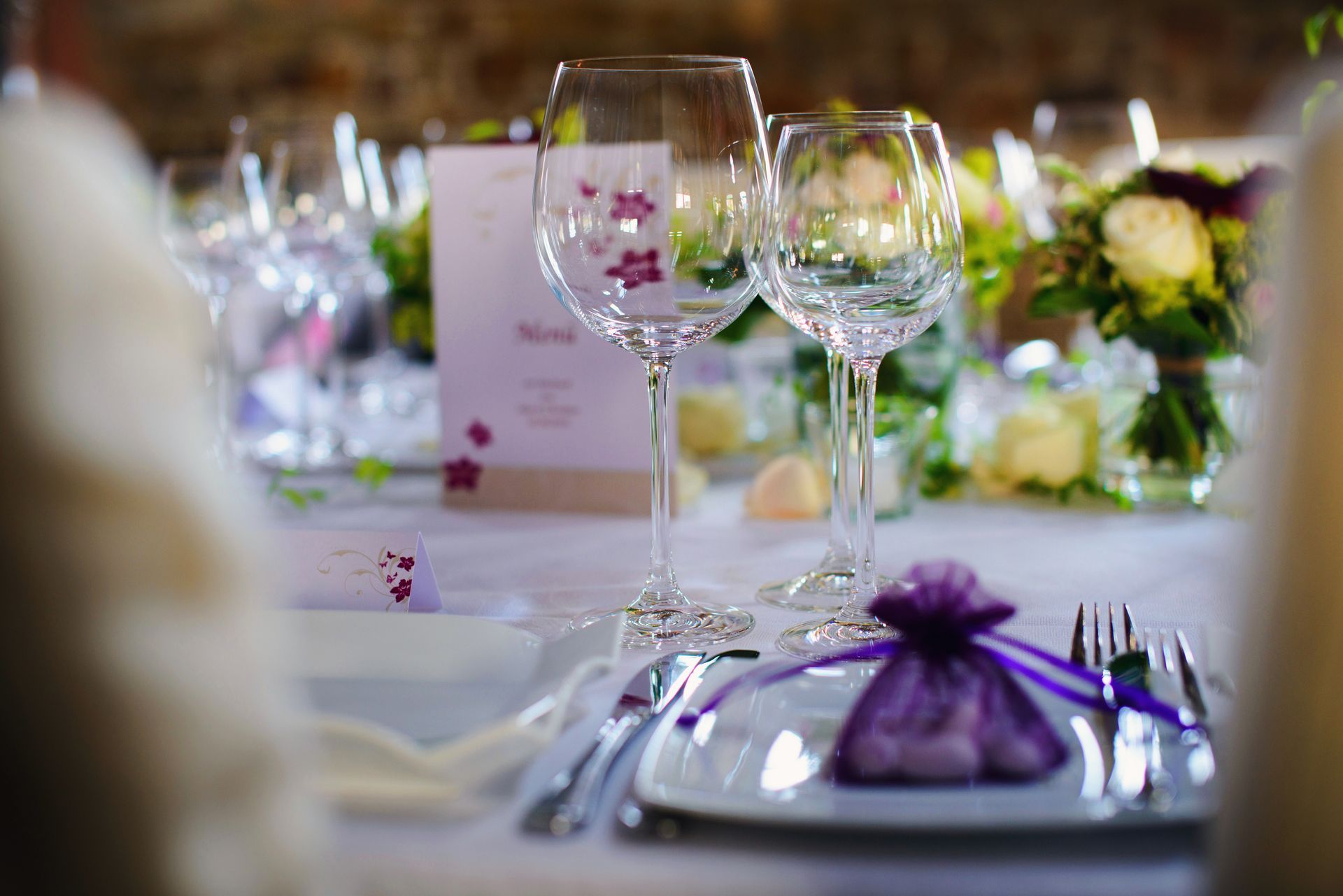 Décoration de table élégante avec verres à vin, ronds de serviette violets et centres de table floraux lors d'un événement formel.