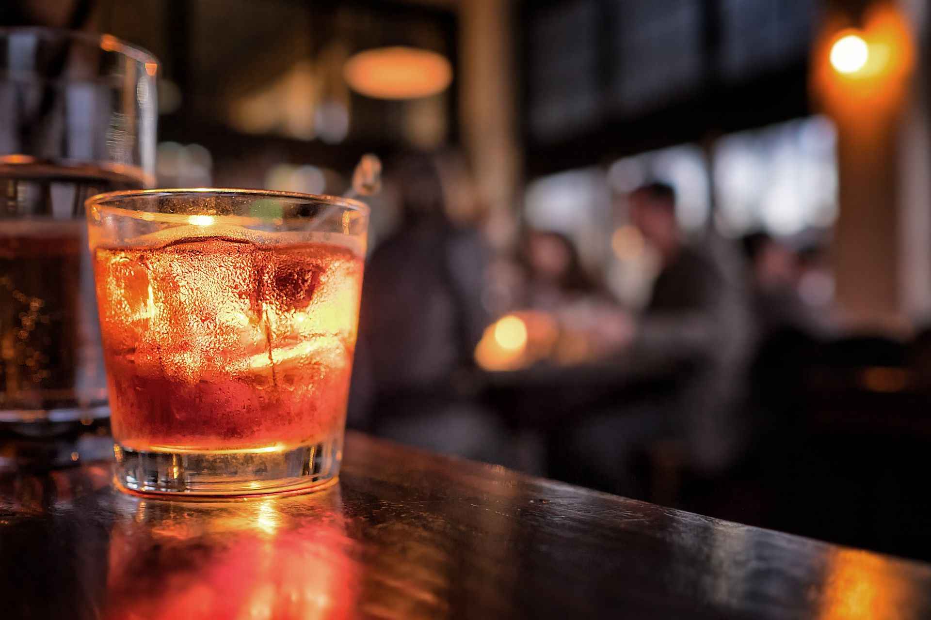 Un verre de whisky incandescent sur un bar, avec des clients flous en arrière-plan.