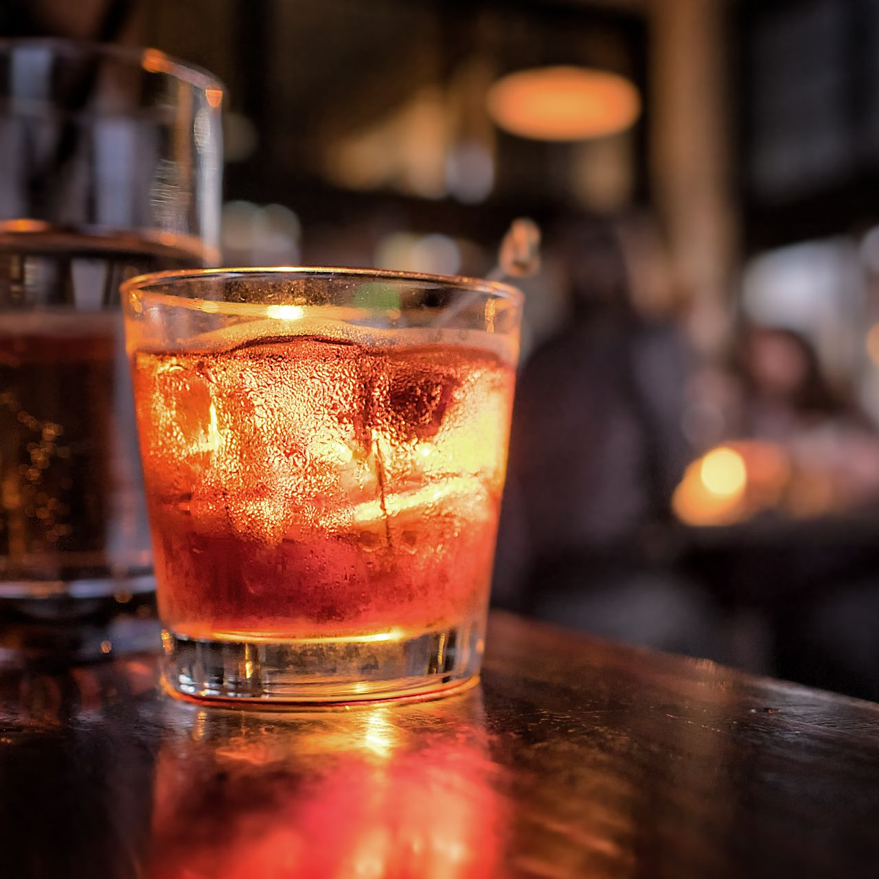 Un cocktail ambré servi dans un verre bas, illuminé sur un bar baigné d'une lumière chaude et diffuse.
