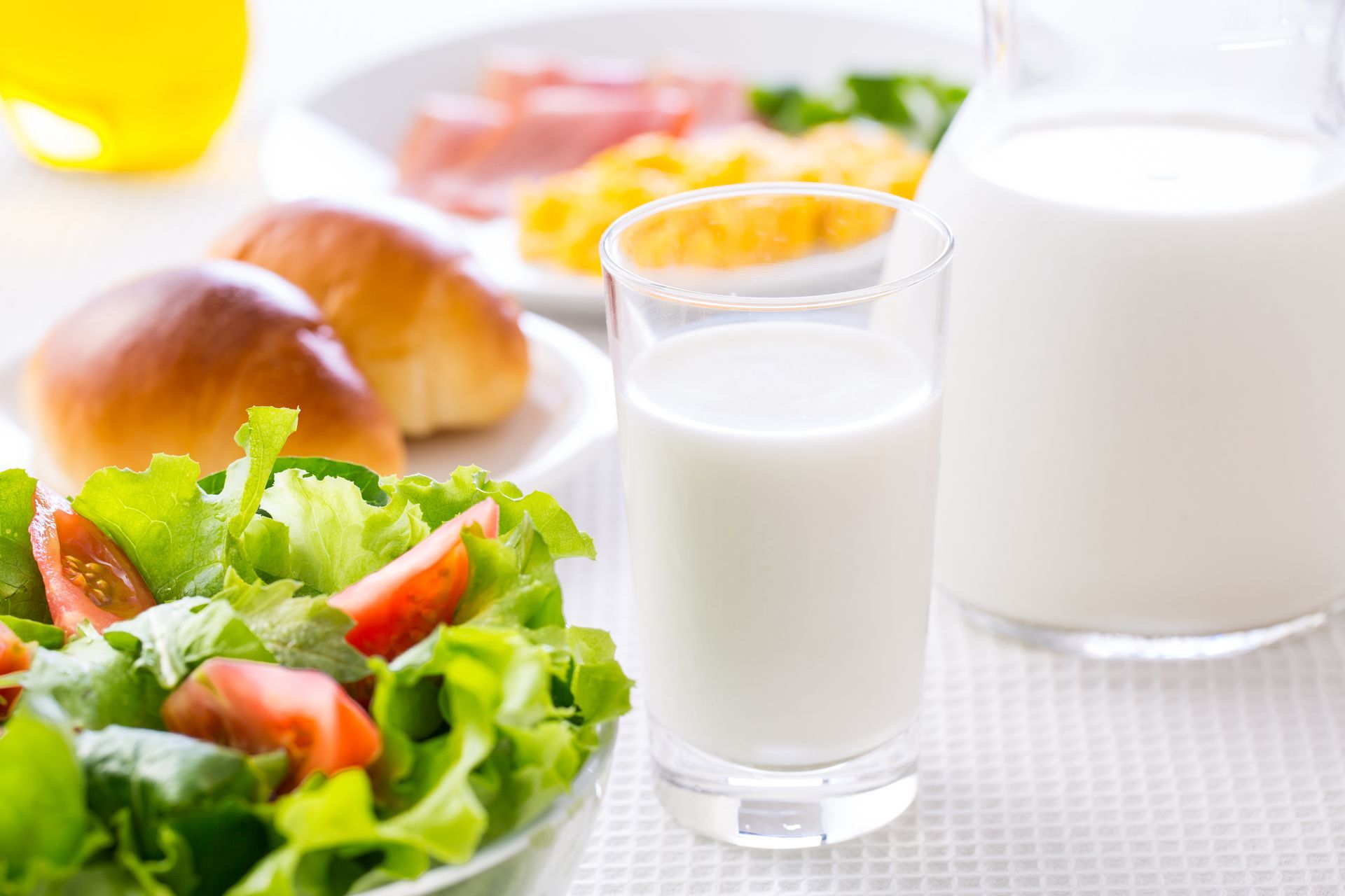 Petit-déjeuner composé de salade, de petits pains, de yaourt, d'un verre et d'un pichet de lait.