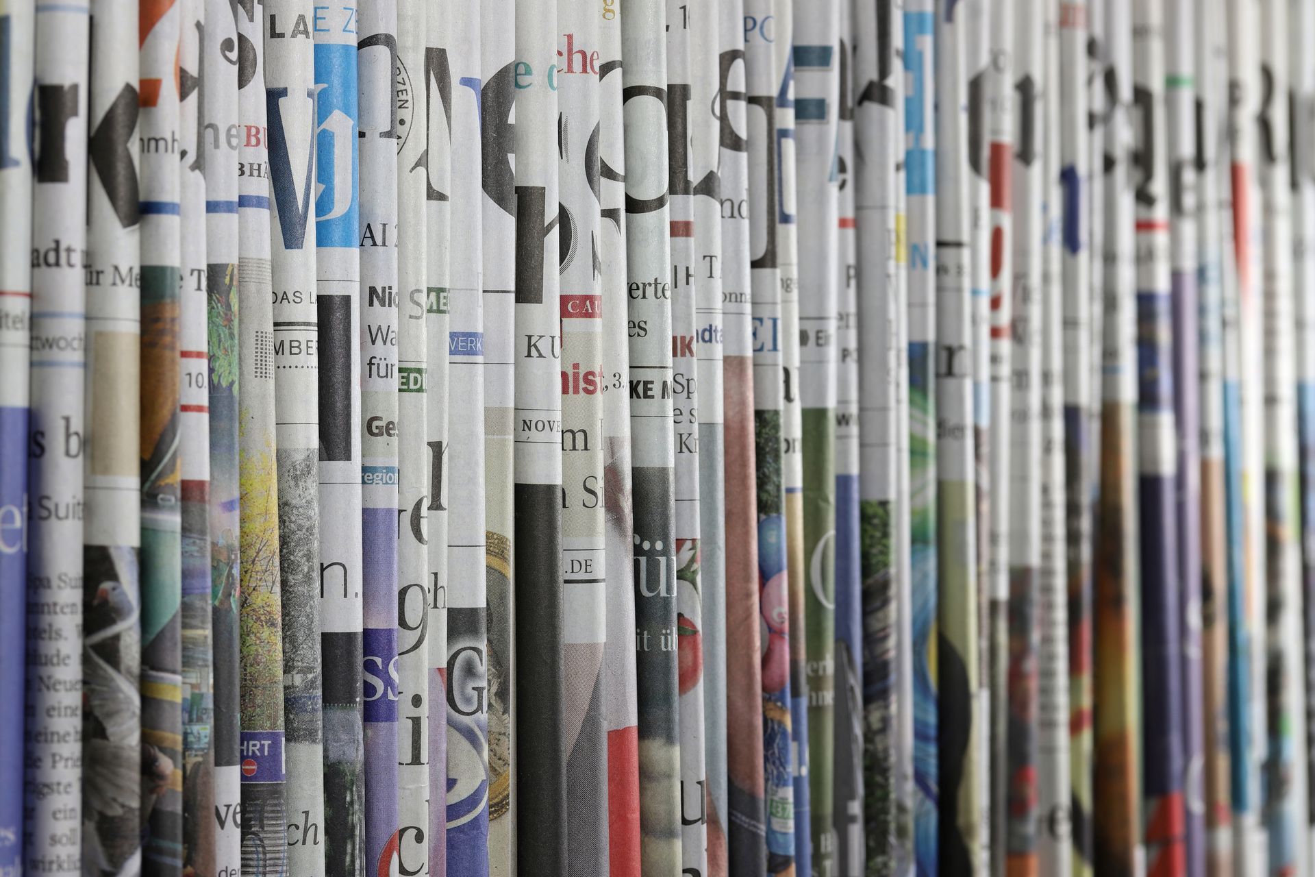 Des rangées verticales de journaux roulés avec des titres et des images colorés, créent un motif texturé.