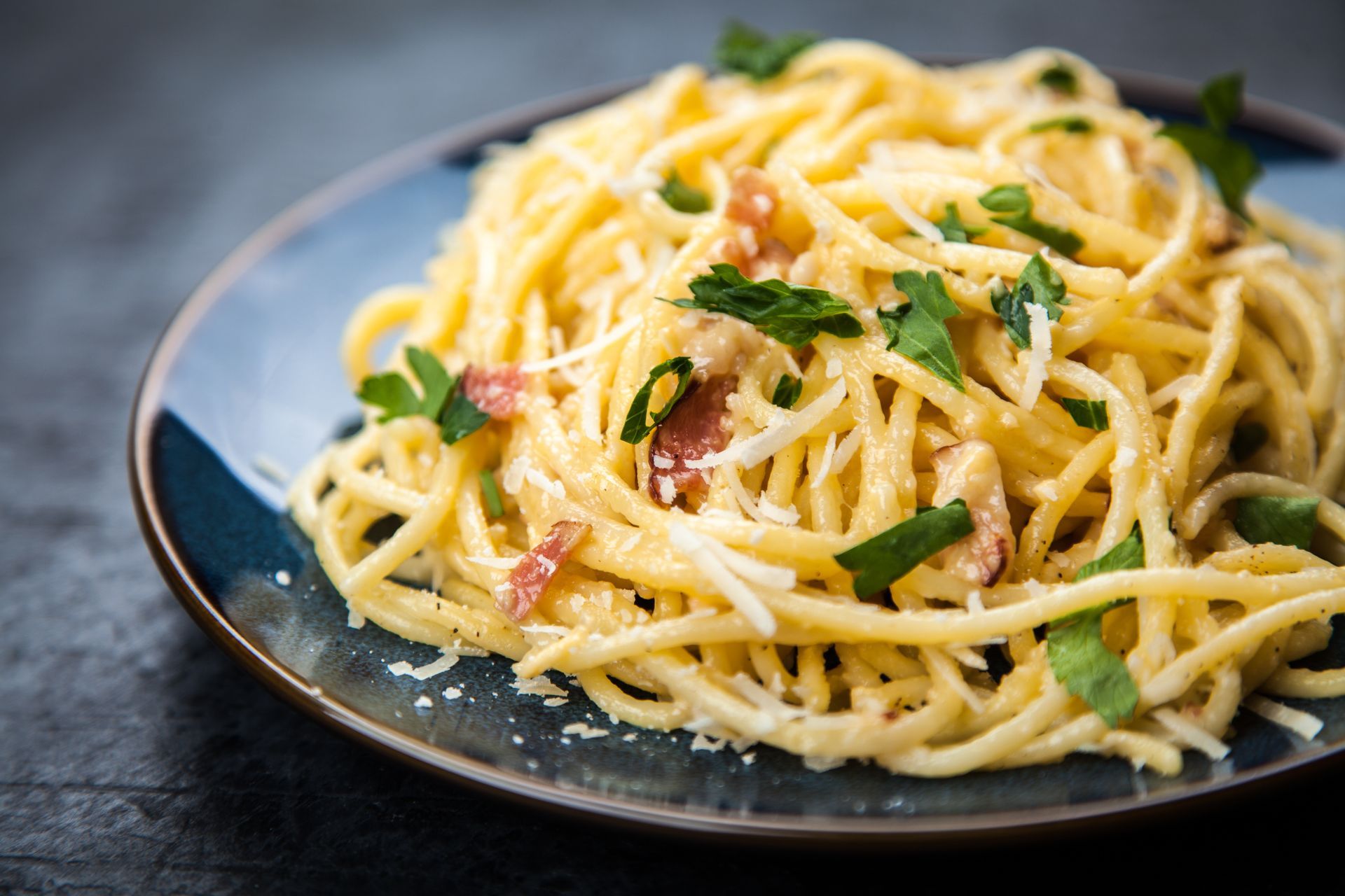 Spaghettis à la carbonara garnis de persil et de lardons, servis sur une assiette bleue.