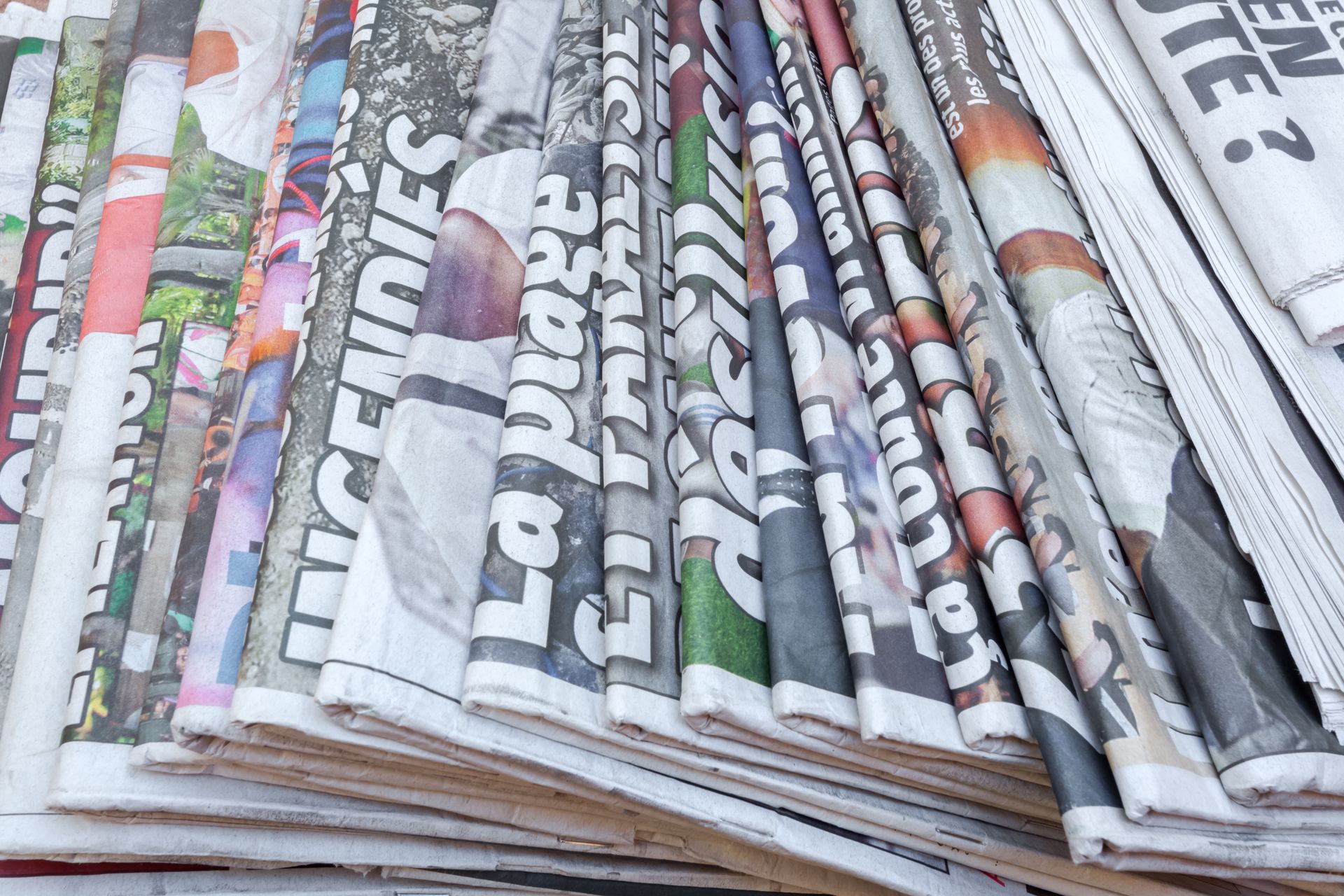 Des journaux roulés et empilés avec des titres visibles et des pages en couleur.
