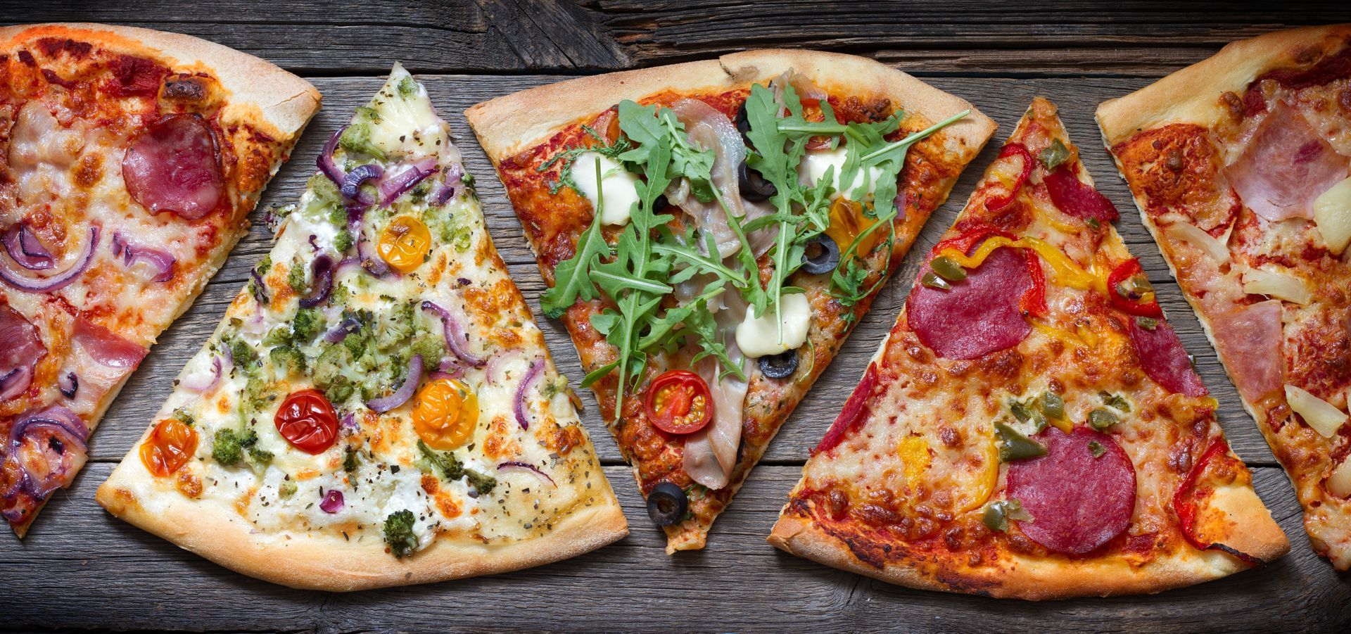 Assortiment de parts de pizza avec différentes garnitures sur une planche en bois rustique.